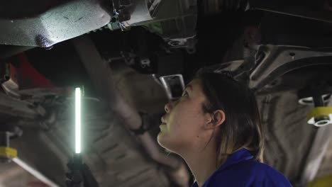 mecánica femenina usando una lámpara led y trabajando debajo de un automóvil en una estación de servicio de automóviles