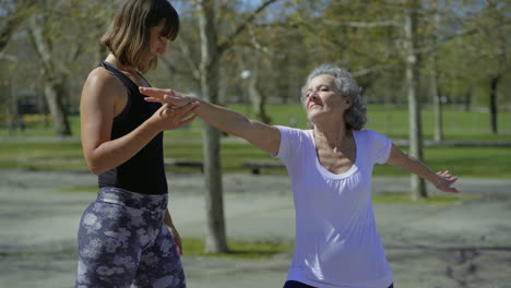 una mujer mayor alegre y una mujer joven practicando yoga en el parque.