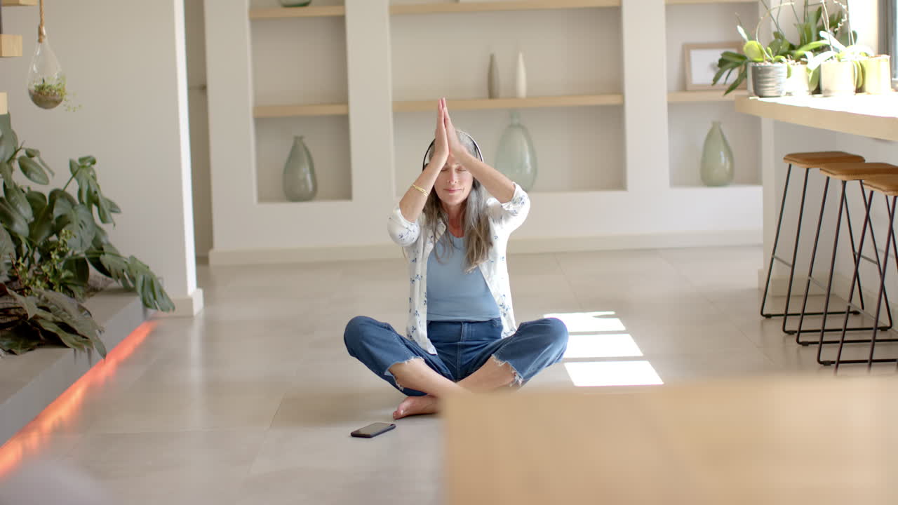Donna caucasica matura che pratica yoga, con smartphone nelle vicinanze