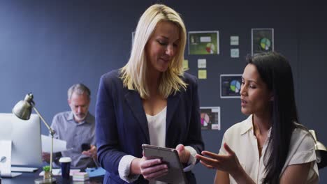 diverse businesswomen using digital tablet discussing in office male colleague behind