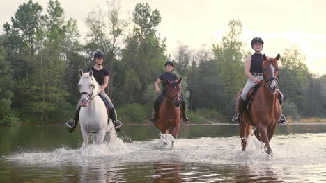 three rider girls crossing the river riding their horses, handheld shot