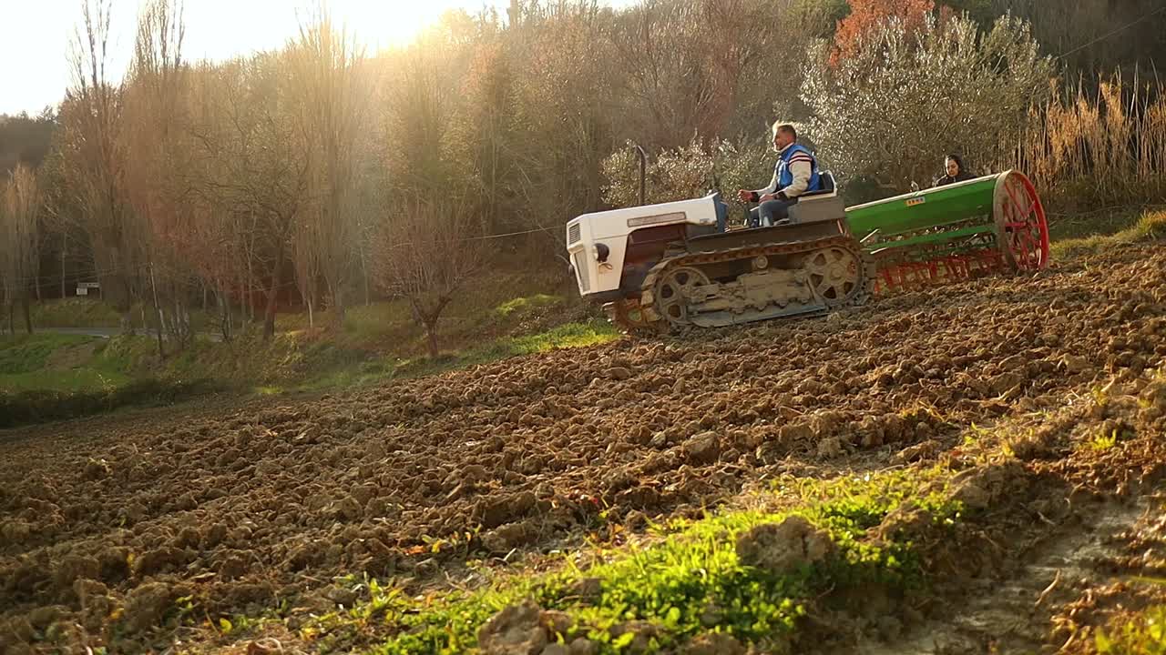 crawler tractor and seeder moving down on the land field at sunset, slow motion medium shot