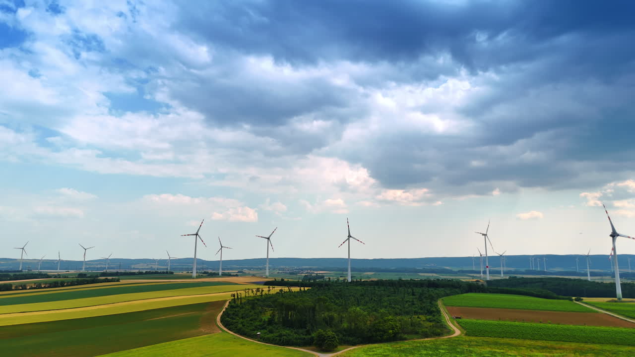 Agricultural plantations with rotating wind mills. Rainy cloudscape covers the sky over the scenery