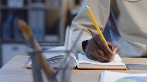 close up view of young man working, making notes in the notebook and drinking coffee in the office at night