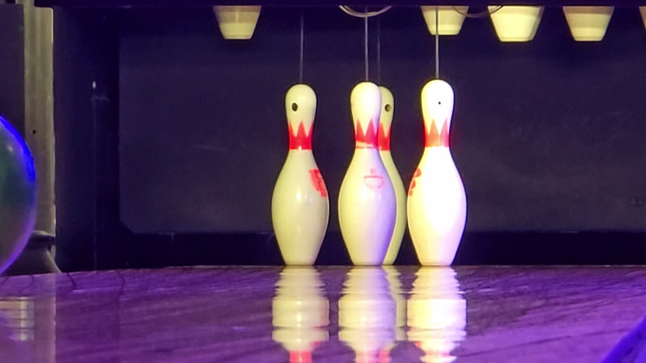 Static shot of bowling pins at the end of the lane as a bowling ball approaches and falls into the gutter