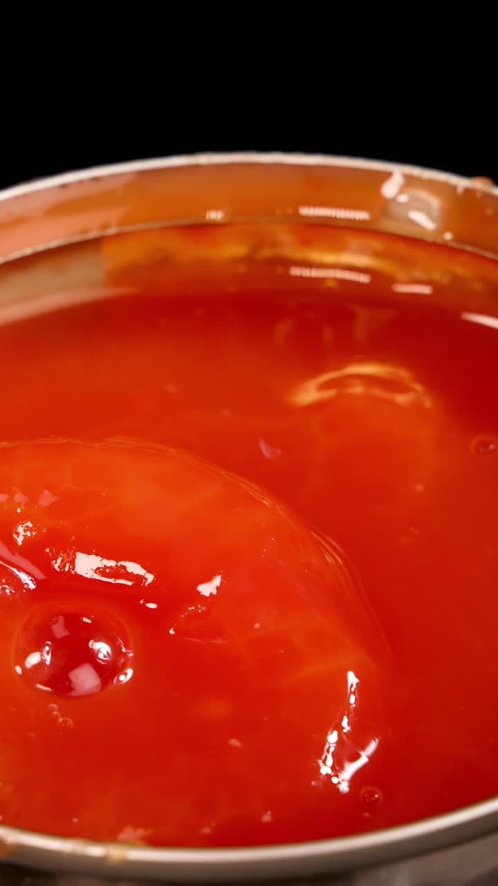Un pomodoro intero pelato schizza in una lattina piena di salsa di pomodoro, ripreso in primo piano con una luminosa illuminazione da studio e un'angolazione della telecamera fissa