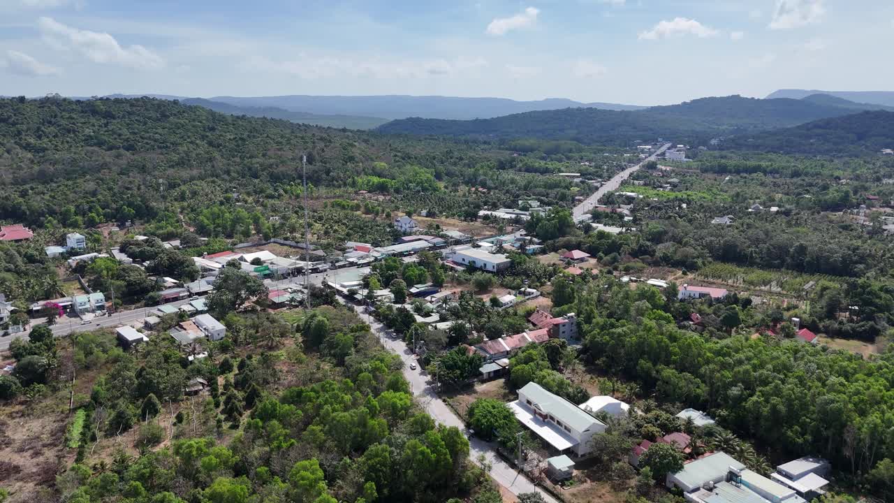 This aerial shot captures a landscape where a straight road extends road are houses and buildings, indicating a residential presence within the lush environment. a sky above is partially cloudy
