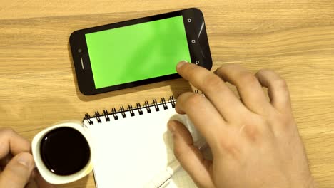 the specialist is sitting at the desk. one hand works with the tablet, the other takes a cup of coffee from the table. green screen.