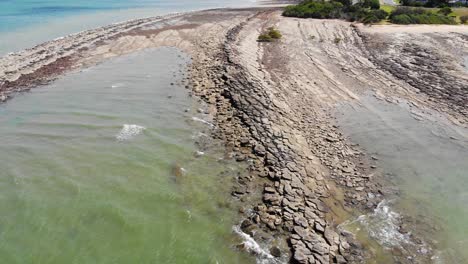 Ein-Funkelnder-Limonengrüner-Und-Arktischer-Blauer-Ozean-Treibt-An-Einem-Wunderschönen-Sonnigen-Tag-Sanfte-Wellen-In-Einen-Strand-Aus-Stein,-Sand-Und-Kleinen-Felsen