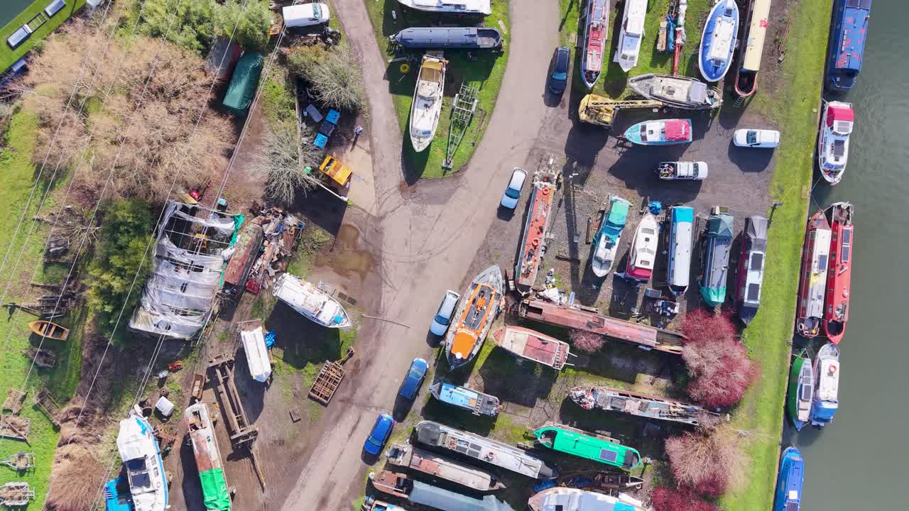 Vue de drone plongeante au-dessus de la marina de Stanstead Abbots dans le Hertfordshire, au Royaume-Uni, volant vers l'avant au-dessus du bâtiment principal et des bateaux à sec, avec la rivière Lea à droite en plein jour.