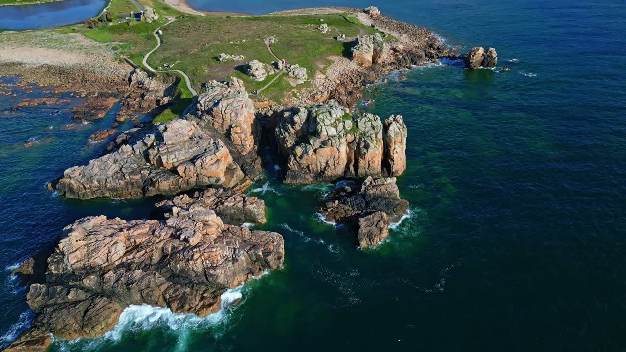 Le Gouffre de Plougrescant, rocky coastline, rugged granite cliffs, clear green water, and coastal path, Brittany, France. Aerial backward tilt-up reveal