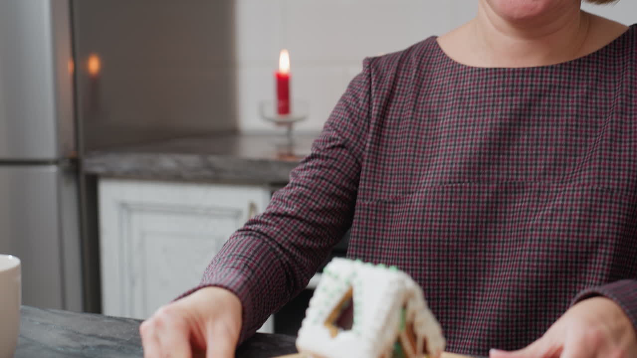 체크 로 된 드레스 를 입은 노인 베이커 는 편안 한 부 에 앉아 나무 트레이 에 장식 된 케이크 를 부드럽게 회전 시키며, 따뜻 한 불 빛, 색 캐비, 그리고 시골적 인 분위기