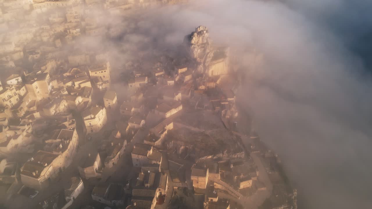 drone shot of old Italian city town - Matera. The city is shrouded with low handing clouds, buildings are visible through them. Warm colours of the rising sun reflected against buildings