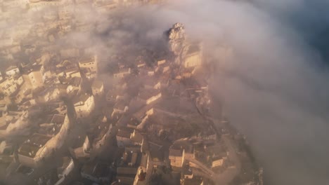 drone shot of old Italian city town - Matera. The city is shrouded with low handing clouds, buildings are visible through them. Warm colours of the rising sun reflected against buildings
