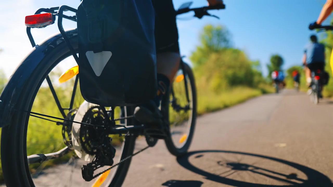 Low-angle close-up of a cyclist pedaling legs and rear wheel on a paved section of the EuroVelo 10 cycle route in the Danish countryside on a sunny summer day