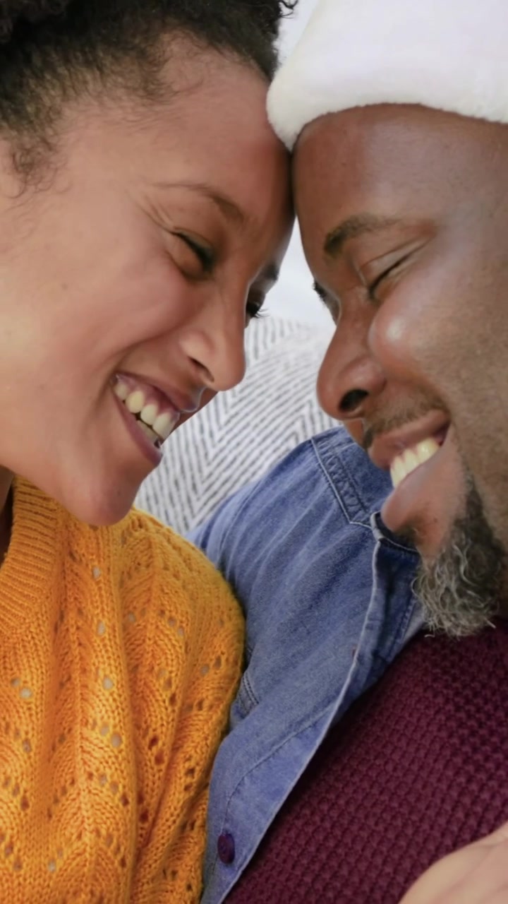 Video verticale: Donna che si appoggia a un uomo, coccolandosi e sorridendo sul divano di casa, con cappello di Babbo Natale, anello, condividendo la gioia.