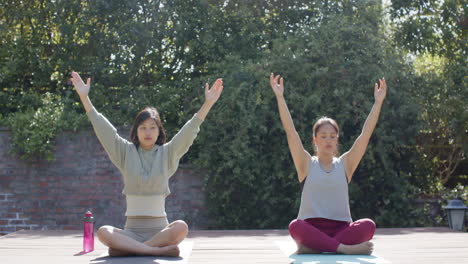 Amigas-Asiáticas-Enfocadas-Practicando-Meditación-De-Yoga-En-Una-Terraza-Soleada,-Cámara-Lenta