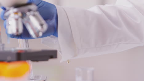 primer plano de un trabajador de laboratorio agregando líquido azul a una diapositiva para su análisis bajo microscopio