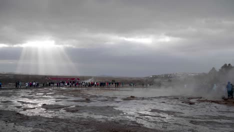 Static,-wide-shot,-of-lots-of-people-watching-the-erupting-geisir,-on-a-cloudy,-autumn-day,-in-Geysir,-Iceland