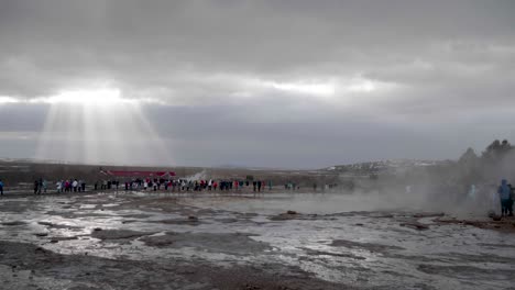 estático, plano general, de mucha gente mirando el geisir en erupción, en un día nublado de otoño, en geysir, islandia