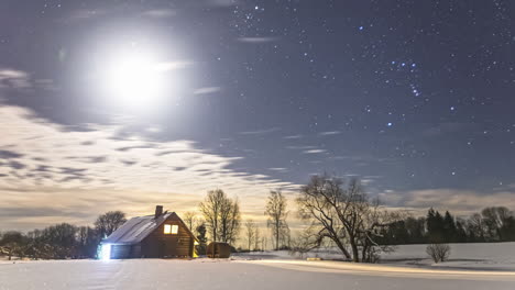 Timelapse-shot-of-a-wooden-cabin-during-beautiful-snowy-night-with-full-moon-and-white-clouds-moving-in-sky