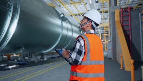 ingeniero asiático con casco de seguridad diseño de turbina eólica plano en una tableta en la fábrica de fabricación de tubos