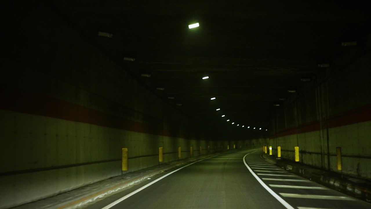 POV di un'auto che guida lentamente attraverso un tunnel buio e lungo di notte.