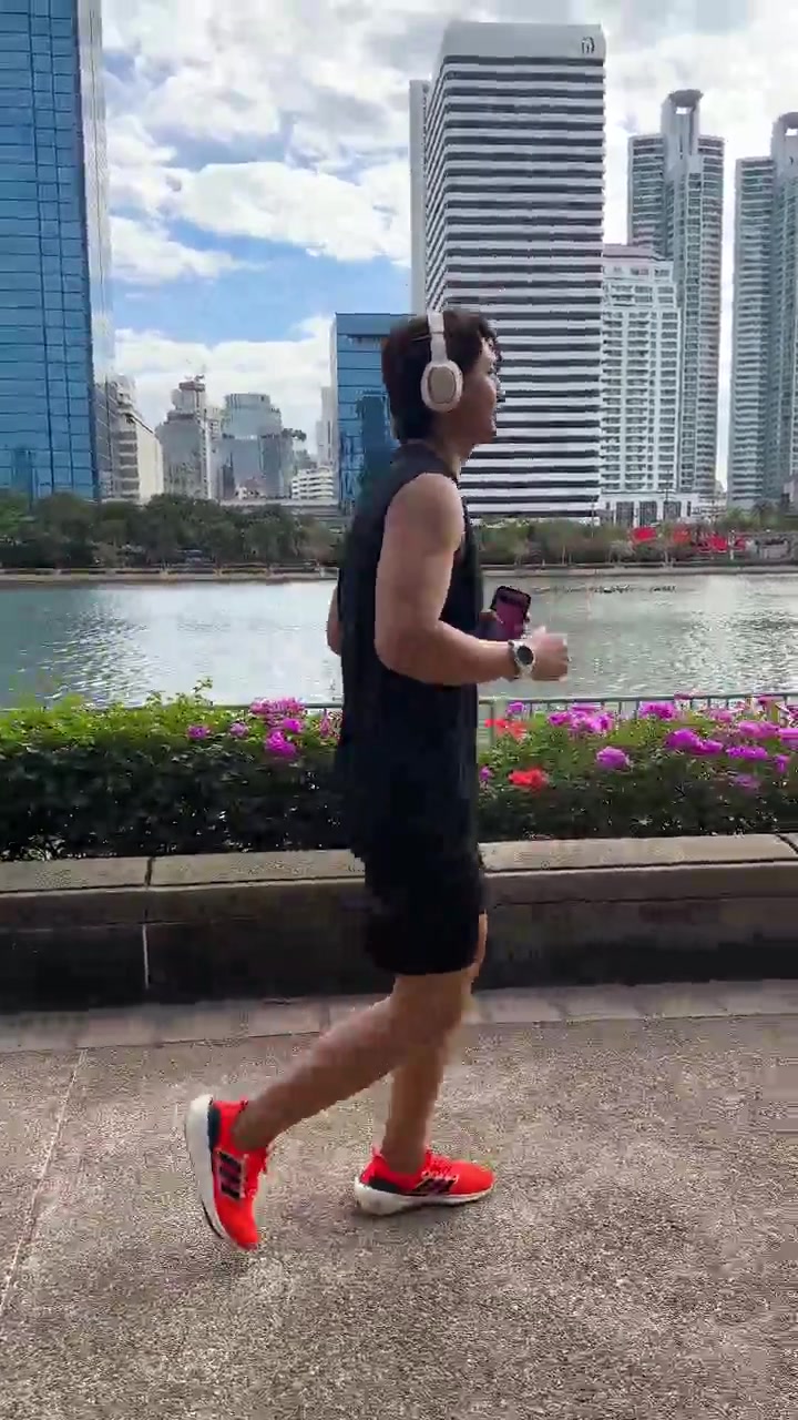 Uomo attivo fa jogging con cuffie e smartphone lungo un sentiero soleggiato di un parco urbano sul lungomare