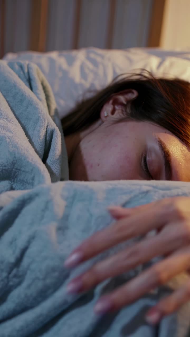 A serene close-up video of a person sleeping under a soft blanket, captured from a side angle