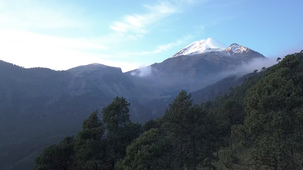 Drone flight rising out of the trees with Pico de Orizaba, the third tallest mountain in North America, coming into view over the treetops just after sunrise