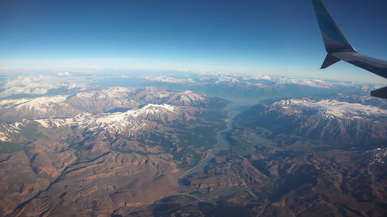 Gliding during cruise, window showing aerial view over snow peaks, winding river, winglet visible