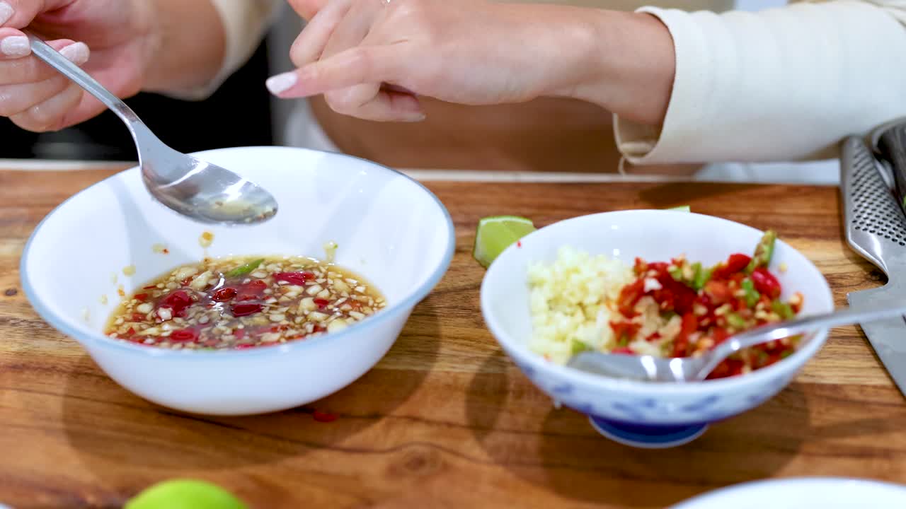 Hands mix fish sauce with garlic and chili in a kitchen setting, showcasing culinary preparation techniques
