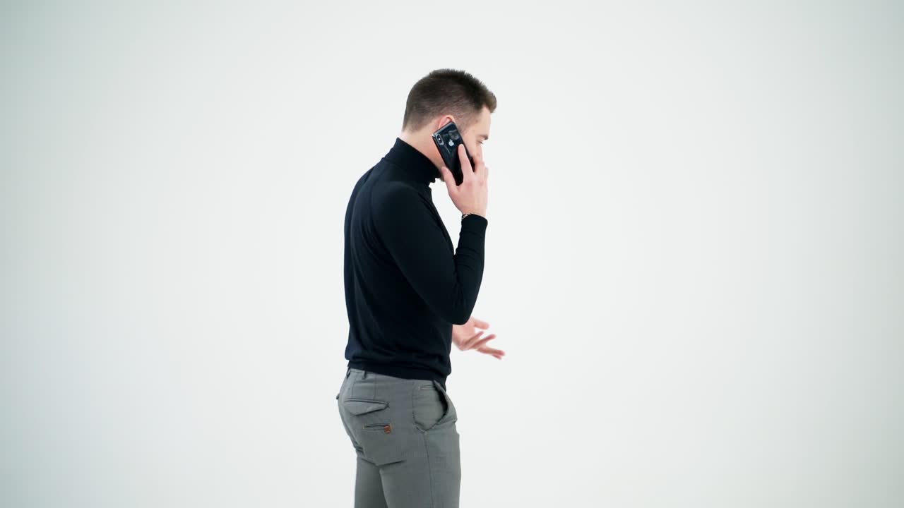 Handsome man having phone talk indoors. Serious young businessman talking on a cellphone and moves slowly isolated on white background. Slow motion.