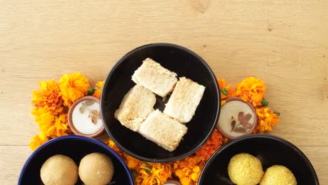 tilt up close up across indian sweets, flowers, diyas on a wooden background for hindu festival of lights, dusshera and diwali preparation and celebration ingredients