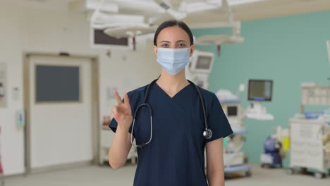 happy indian female doctor showing victory sign with mask on