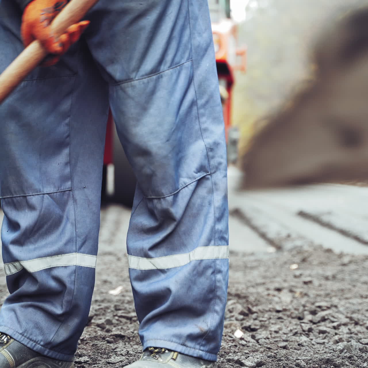 Team of workers put the hot asphalt on a street on the background of steamroller. Road construction workers with shovels in protective uniforms.