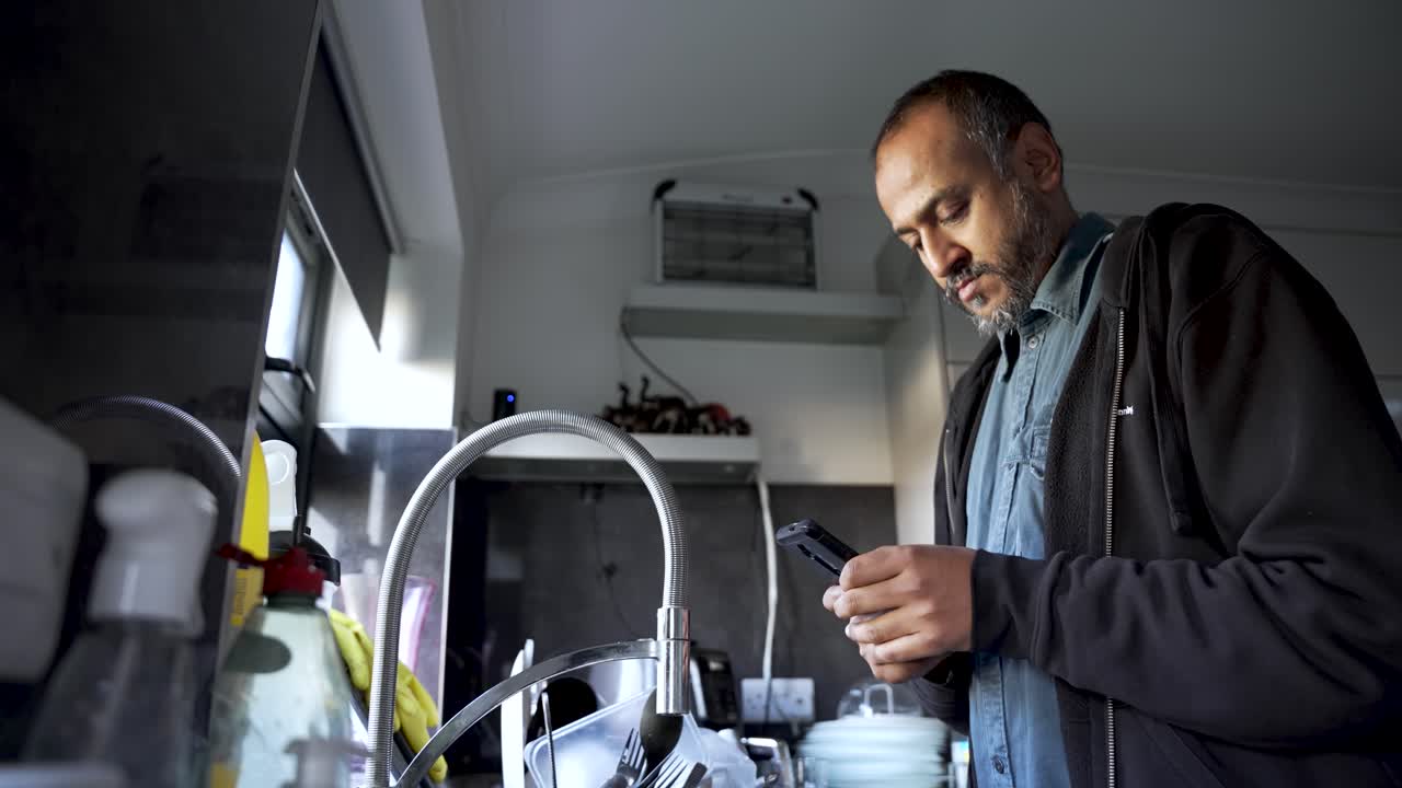 South Asian Man Using Mobile Phone Near Kitchen Sink Checking Messages Browsing Internet Mobile App Social Media Communication
