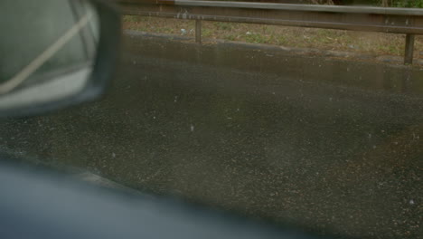 vehicle driving on wet asphalt during rainfall, side view from inside car