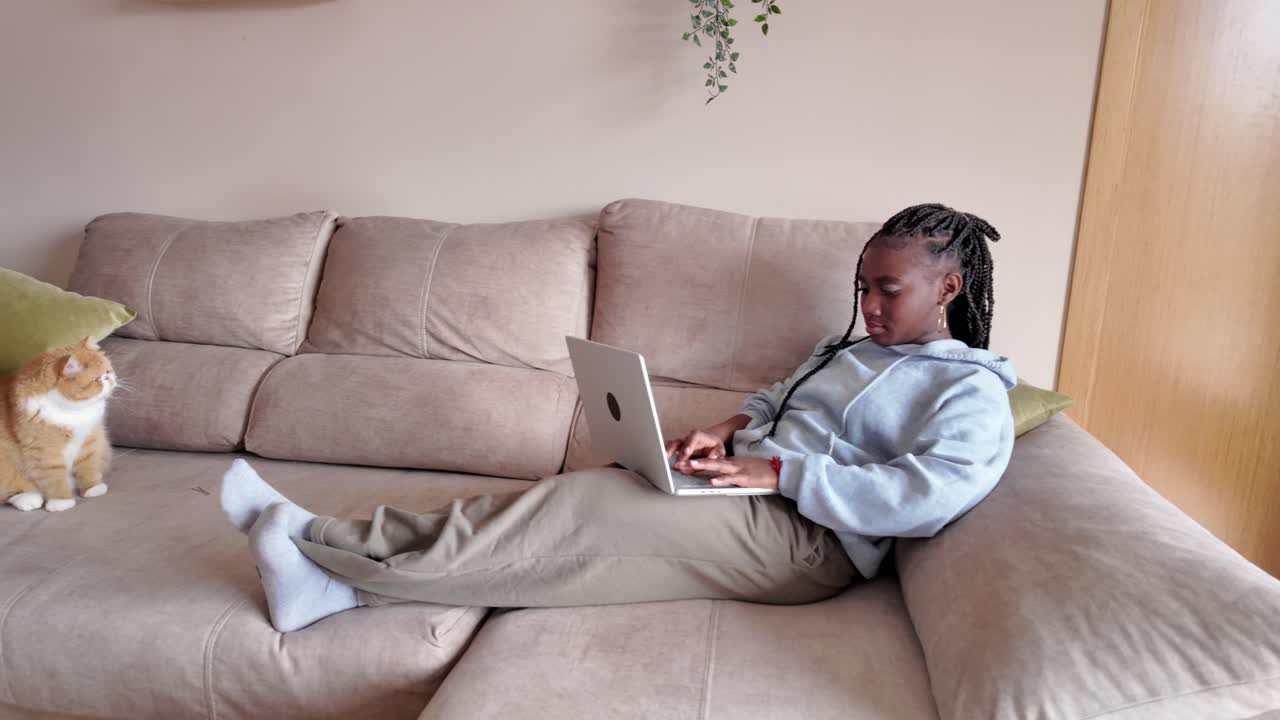Woman using laptop on couch with cat