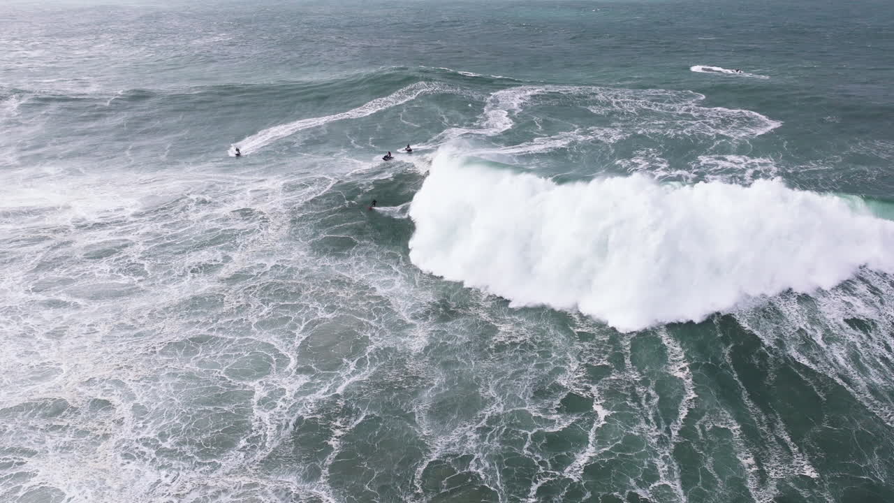 Aerial drone shot of big wave surfer surfing a giant wave and celebrating in Nazare, Portugal, Europe. Nazaré, big wave surfing town with biggest waves in the world. Professional tow-in with jet ski