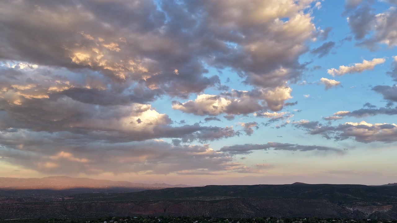 Timelapse 4K con drone di un clima mutevole e una lunga coltre di nuvole al tramonto. Un sistema meteorologico dinamico si muove attraverso un vasto cielo, proiettando un'onda luminosa e increspata su una cima di canyon desertico elevato