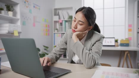 young asian businesswoman sit on desk with laptop overworked tired burnout syndrome at office.