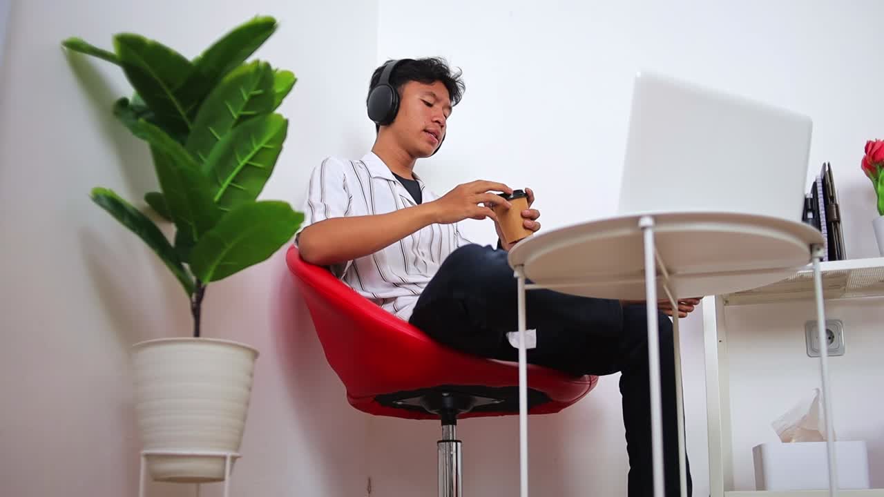 Young professional taking break sipping coffee while listen music on laptop