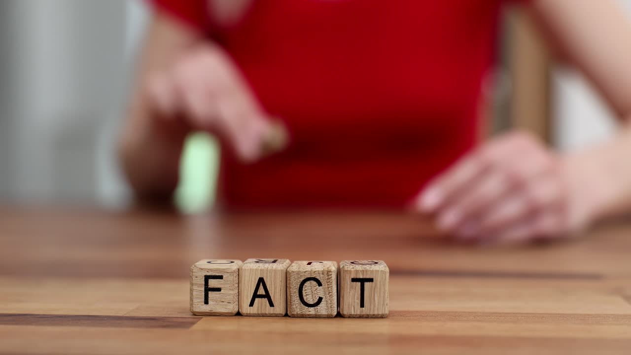 A person spelling the word FACTS using wooden alphabet blocks