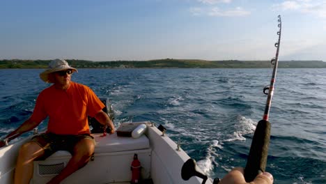 First-person-pov-of-man-fishing-with-rod-and-another-fisherman-trolling-fishing-with-line-while-holding-steering-tiller-of-moving-motorboat-in-background