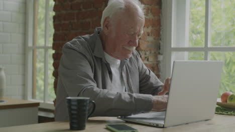 senior man using laptop in kitchen