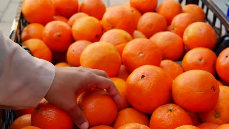 a hand picking fresh oranges from a basket