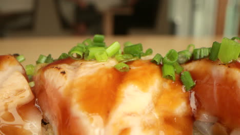 chopped onion chives on top of salmon sushi rolls with sauce served in a sushi restaurant - macro, slow tracking shot