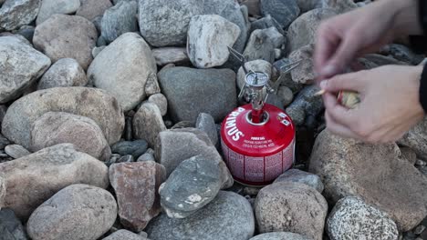 Person-lighting-a-gas-stove-using-matches-while-wildcamping,-close-up-shot