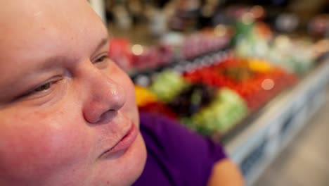 close-up shot: happy overweight man in purple t-shirt eating croissant in supermarket. face of an overweight man eating sweets in a supermarket